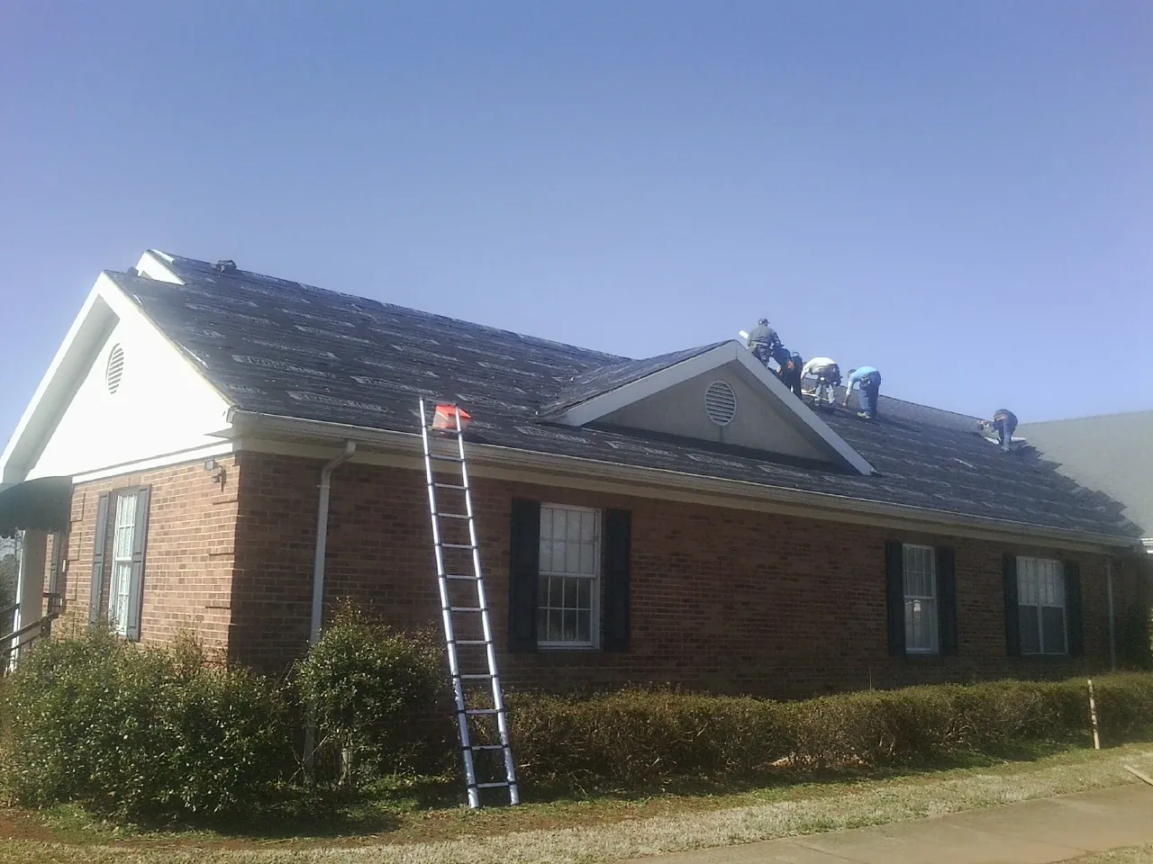 Crew tearing shingles off a brick ranch roof with a ladder set — Emergency Roof Repair work by our crew in Cotati
