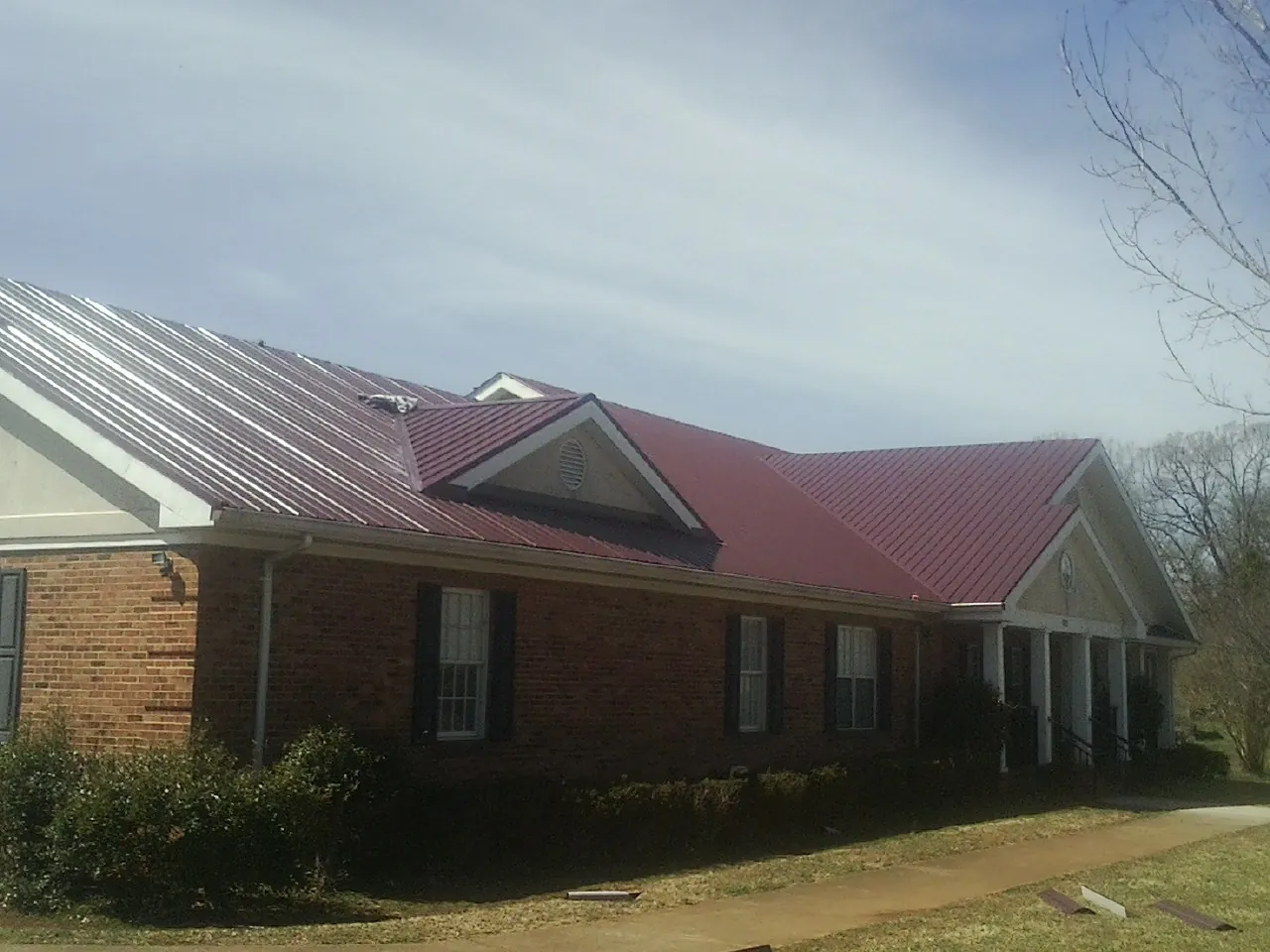 Red metal roof with gabled entries on a long brick building, from a Hail Damage Roof Repair job in Cotati