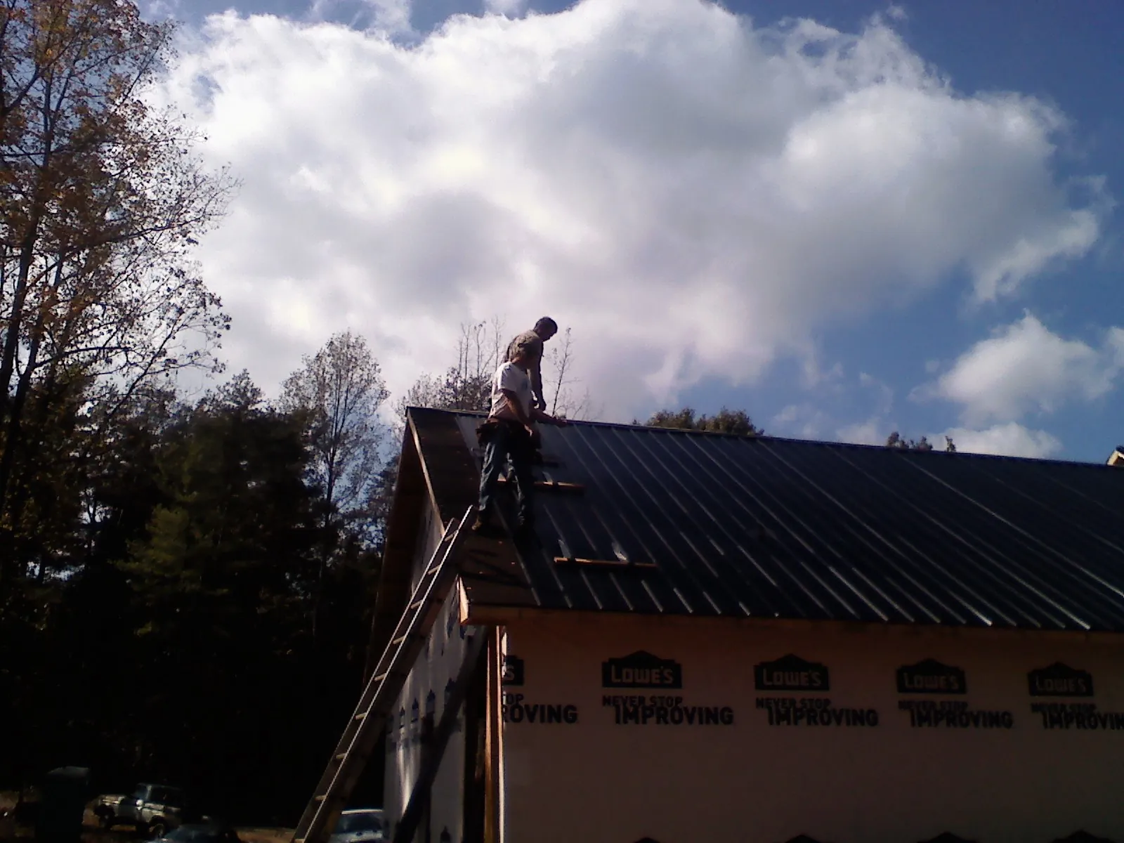 Roofer fastening dark metal panels high against a cloudy sky, from a Roof Inspection job in Cotati